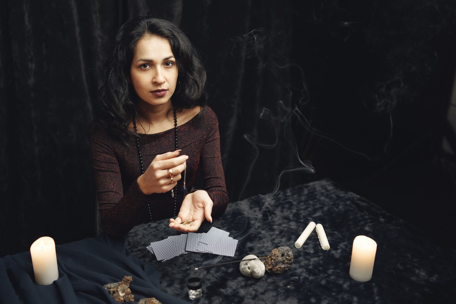 A mysterious woman in dark attire reading tarot cards surrounded by candlelight and mystical objects.